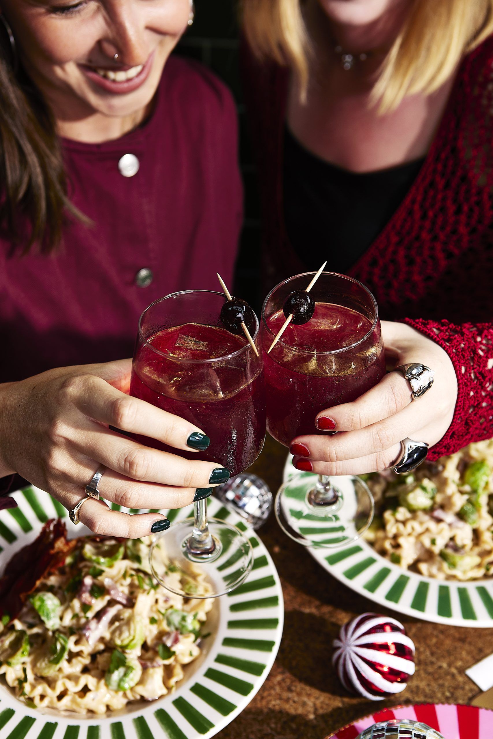 Two people enjoying an Italian meal of pasta, cheersing with a festive cocktail. 