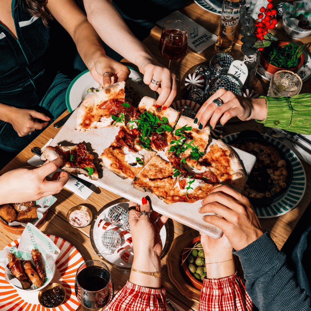 A group of people enjoying a Christmas party at ASK Italian restaurants, with everyone tucking into a festive special pizza. 