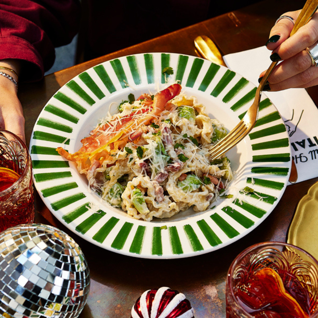 Somebody digging into bowl of pasta carbonara with brussels sprouts and a crispy piece of pancetta. 