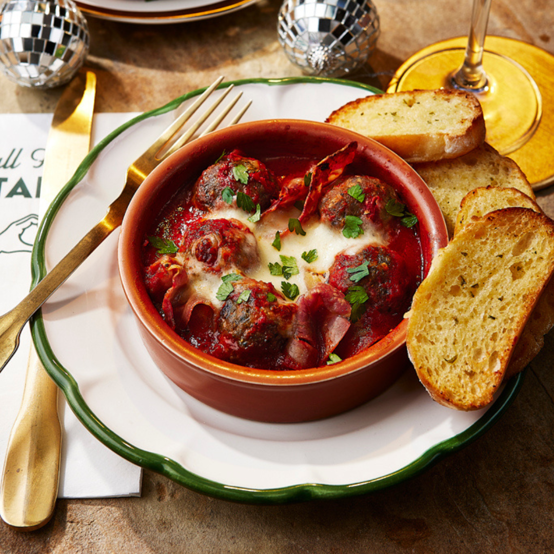 A plate of festive meatballs served at ASK Italian restaurants. The meatballs are served in a red tomato sauce with bubbling mozzarella on top. 